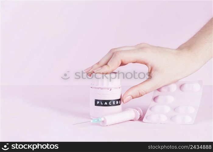 human hand placebo bottle with syringe pills blister pink background