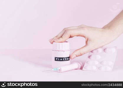 human hand placebo bottle with syringe pills blister pink background