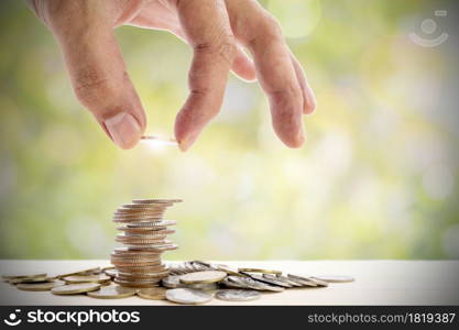 Human hand placing a coin on a pile of coins, use for for business and financial growth concepts.