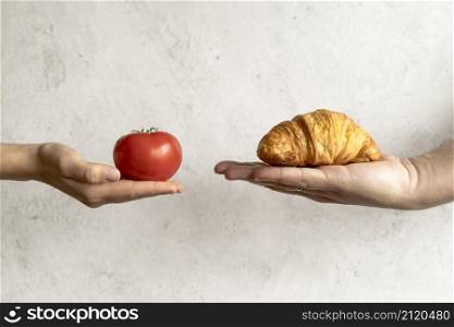 human hand showing croissant red tomato front concrete background