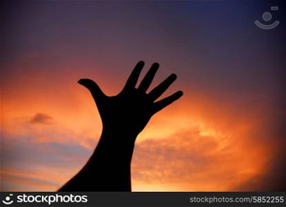 human hand trying to reach the sky at sunset