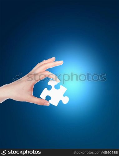 human hand with a blue shining piece of puzzle
