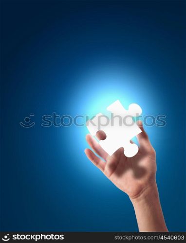 human hand with a blue shining piece of puzzle