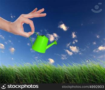 Human hand with green watering pot watering green grass