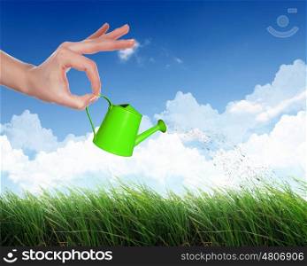 Human hand with orange watering pot watering green grass
