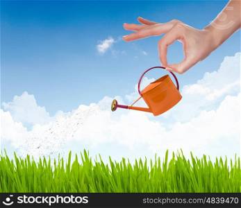 Human hand with orange watering pot watering green grass