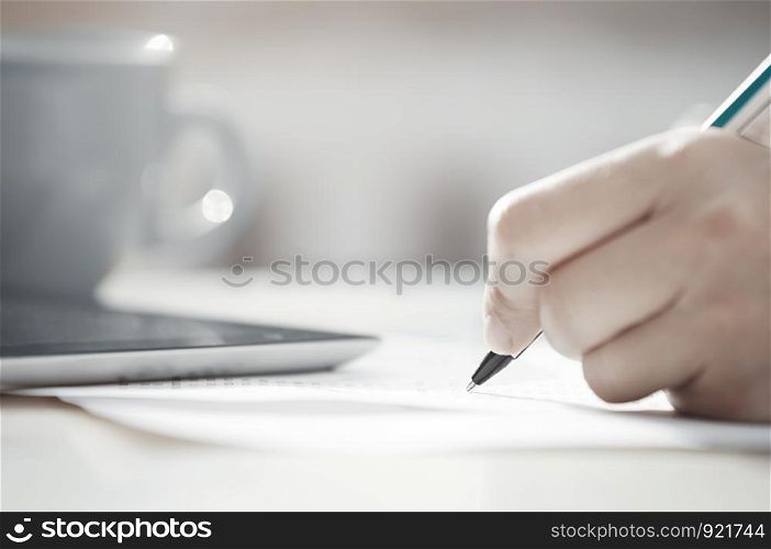 Human hand with pen calculating budget. Teacup and digital tablet on a table