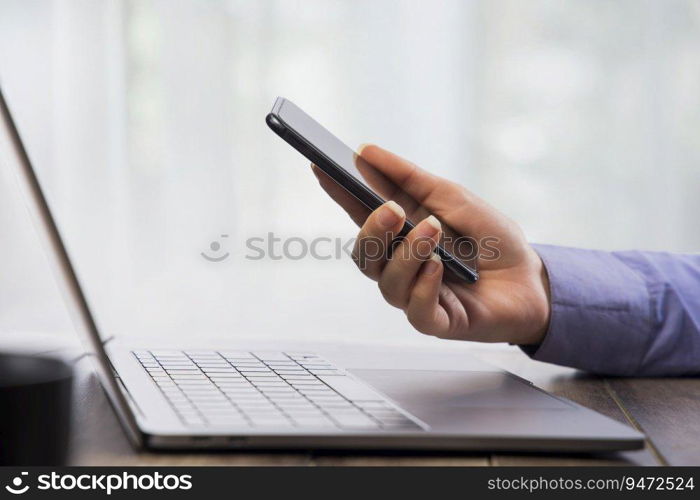 Human hand working on phone with a laptop in front.