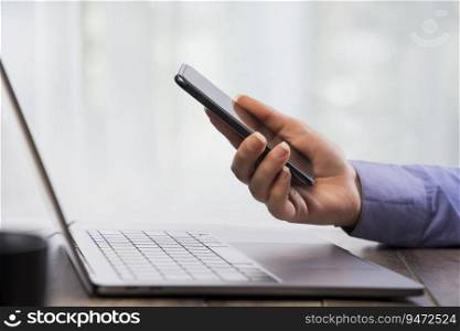 Human hand working on phone with a laptop in front.