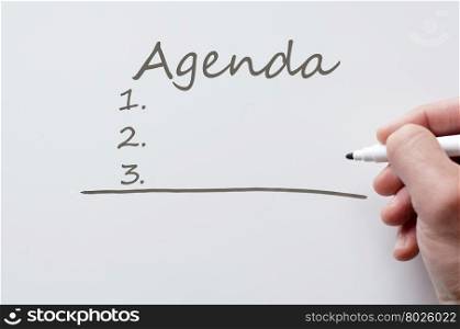 Human hand writing agenda on whiteboard