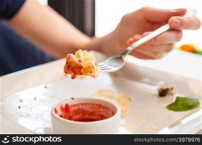 Human hands at dinner table holding fork eating pancake with strawberry sauce, meal is finished.