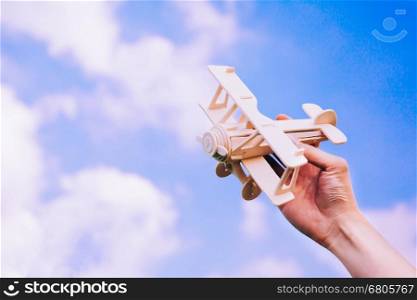 Human hands holding a wooden plane toy over blue sky with copyspace