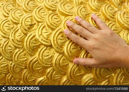 Humand hand touching golden cement plaster in fish skin curve pattern wall background.