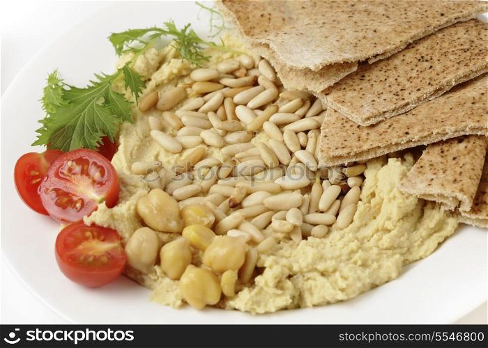 Hummus and lightly roasted pine-nuts dip, garnished with cherry tomatoes and young salad leaves, viewed close-up