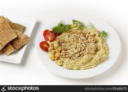 Hummus and pine-nuts dip, garnished with cherry tomatoes and young salad leaves and served accompanied by flat Arab bread, or kubz