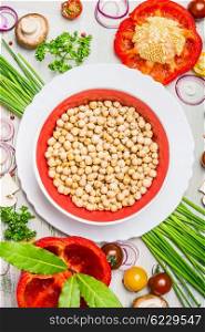 Hummus dish and various vegetables and seasoning ingredients for tasty vegetarian cooking on light rustic wooden background, top view composing. Healthy eating and diet food concept.