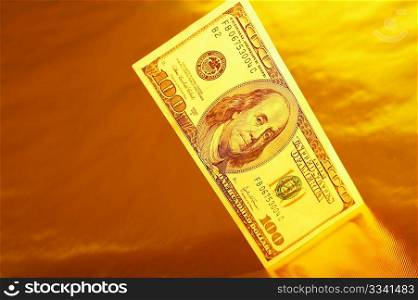 Hundred dollar denomination stands on a reflecting surface of a gold background