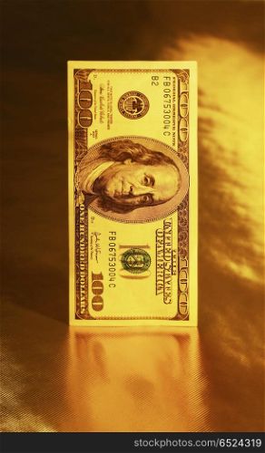 Hundred dollar denomination stands on a reflecting surface of a gold background. Steady currency