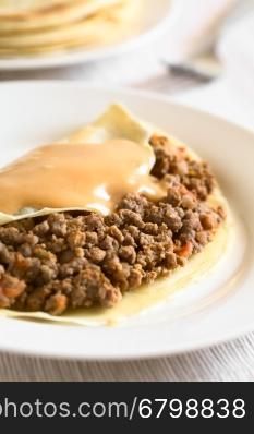 Hungarian Hortobagyi Palacsinta or Crepe a la Hortobagy, a savory thin pancake filled with minced meat and served with a paprika and sour cream sauce based on the sauce of the meat, photographed with natural light (Selective Focus, Focus in the middle of the crepe)