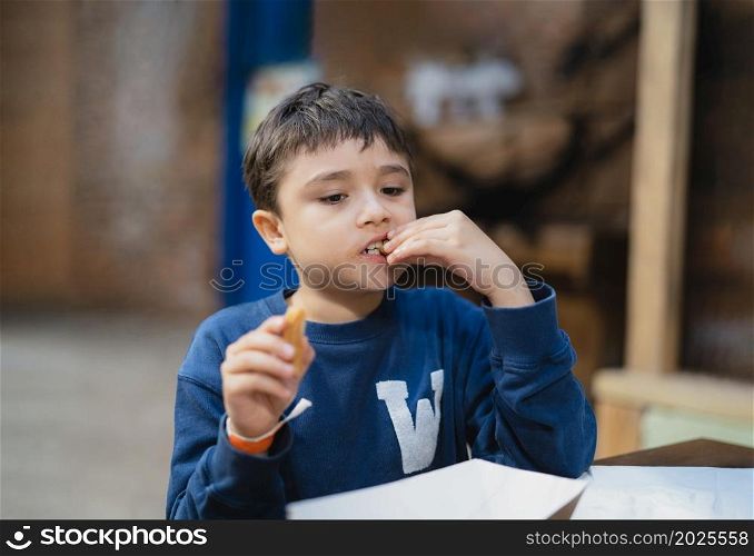Hungry boy eating Churros stick, Schoolkid having snack after lunch in School cafe, Healhty Child sitting in the coffee shop eating meal.