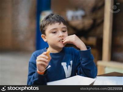 Hungry boy eating Churros stick, Schoolkid having snack after lunch in School cafe, Healhty Child sitting in the coffee shop eating meal.