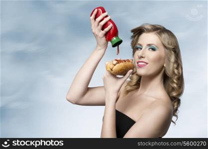 hungry girl with fashion look posing with curly blonde hair putting tomato ketchup on her hot-dog