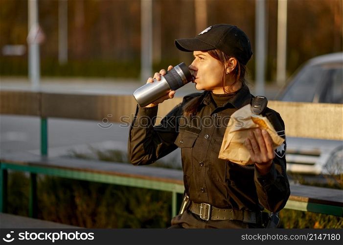 Hungry police woman eating sandwich sitting on park bench. Female cop in uniform take break. Police woman take break eating in park