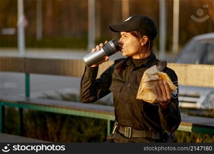 Hungry police woman eating sandwich sitting on park bench. Female cop in uniform take break. Police woman take break eating in park