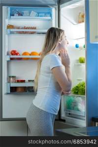 Hungry woman looking inside open fridge at late night