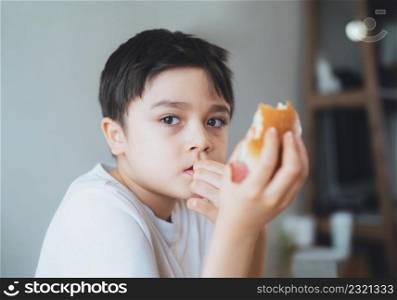 Hungry young boy eating homemade bacon sandwiches with mixed vegetables, Healthy Kid having breakfast at home, Child bitting finger nails and looking out with thinking face