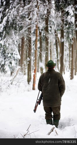 Hunter, armed with a rifel, standing in a snowy forest