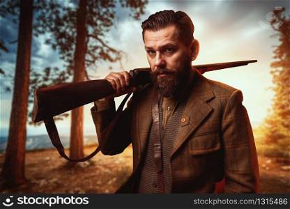 Hunter man in vintage hunting clothing with old gun, forest on background. Hunt lifestyle
