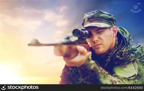 hunting, army, military service and people concept - young soldier, sniper or hunter with gun aiming or shooting over sky background. soldier or hunter with gun aiming and shooting
