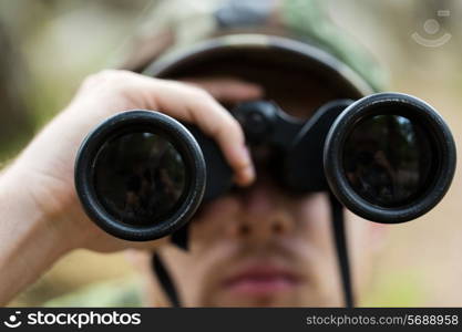 hunting, war, army and people concept - close up of young soldier, ranger or hunter with binocular observing forest