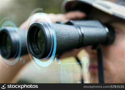 hunting, war, army and people concept - close up of young soldier looking to binocular with virtual hologram and observing forest