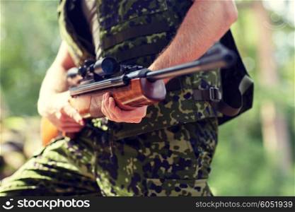 hunting, war, army and people concept - close up of young soldier, ranger or hunter hands holding gun and walking in forest
