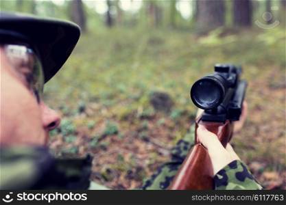 hunting, war, army and people concept - close up of young soldier, ranger or hunter with gun in forest
