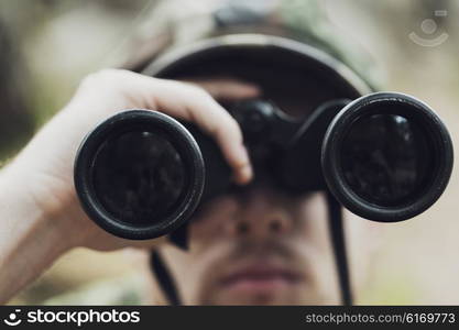 hunting, war, army and people concept - close up of young soldier, ranger or hunter with binocular observing forest