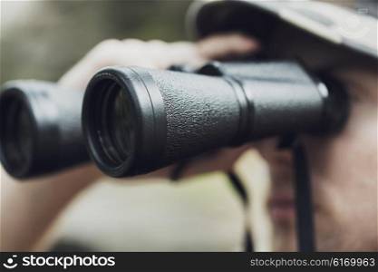 hunting, war, army and people concept - close up of young soldier, ranger or hunter with binocular observing forest