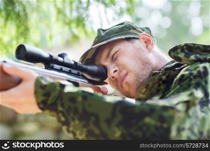 hunting, war, army and people concept - young soldier, ranger or hunter with gun aiming and shooting in forest