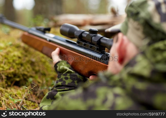 hunting, war, army and people concept - young soldier, ranger or hunter with gun walking in forest