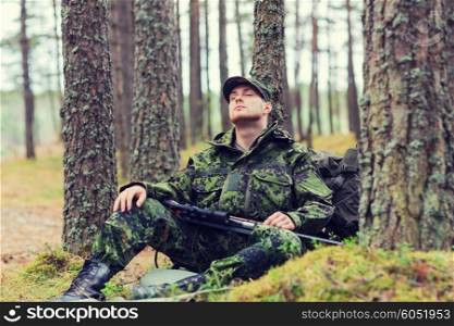 hunting, war, army and people concept - young soldier, ranger or hunter with gun sitting and sleeping in forest