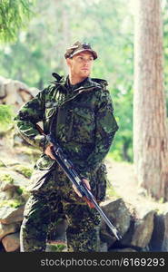 hunting, war, army and people concept - young soldier, ranger or hunter with gun walking in forest