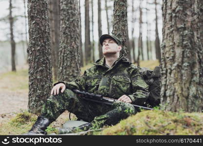 hunting, war, army and people concept - young soldier, ranger or hunter with gun sitting and sleeping in forest