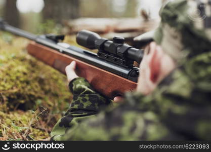 hunting, war, army and people concept - young soldier, ranger or hunter with gun walking in forest