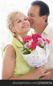 Husband and wife holding flowers kissing and smiling