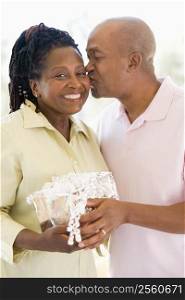 Husband and wife holding gift kissing and smiling