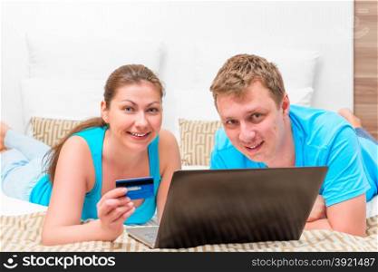 husband and wife with a credit card and a laptop on the bed in the bedroom