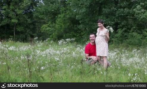 Husband brings flowers for his pregnant wife on the green meadows