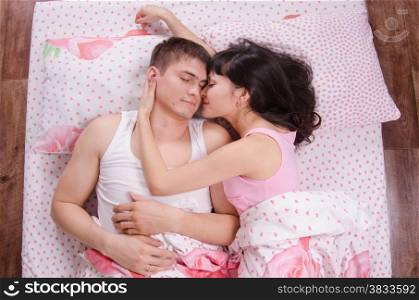 Husband embraces his young wife in bed